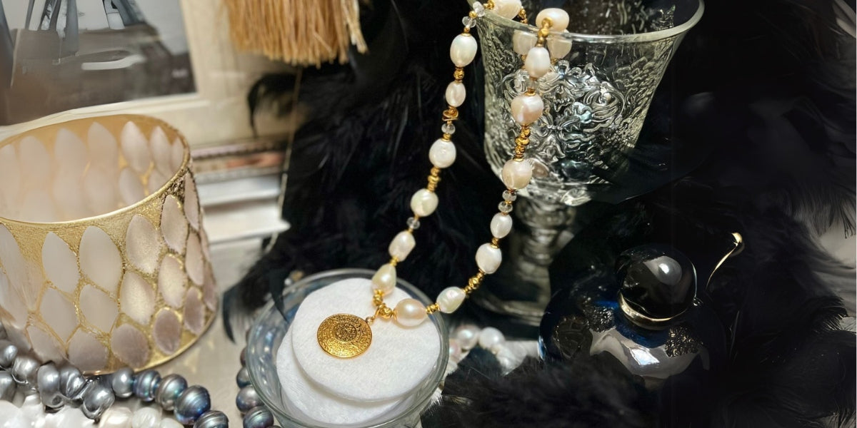 Naszyjnik z pereł naturalnych z monetą Azteków, w otoczeniu perfum, piór i świec. Kolekcja Paris-Paris Meritano Naszyjnik z pereł naturalnych z monetą Azteków, w otoczeniu perfum, piór i świec. Kolekcja Paris-Paris Meritano