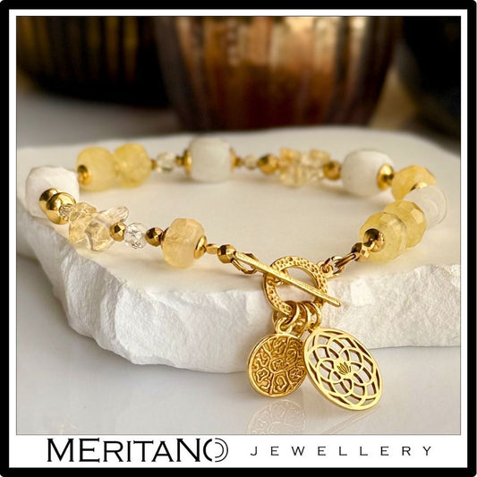 Bransoletka z kamieniem księżycowym i cytrynem, ozdobiona zawieszką, leżąca na kamieniu Bransoletka z kamieniem księżycowym i cytrynem, ozdobiona zawieszką, leżąca na kamieniu