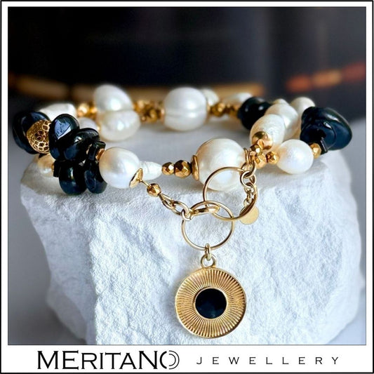 Bransoletka z pereł naturalnych z czarnym turmalinem i złotą zawieszką, leżąca na białym gipsie Bransoletka z pereł naturalnych z czarnym turmalinem i złotą zawieszką, leżąca na białym gipsie