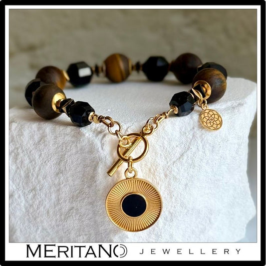 Bransoletka z czarnym turmalinem i tygrysim okiem z zawieszką, leżąca na białym kamieniu Bransoletka z czarnym turmalinem i tygrysim okiem z zawieszką, leżąca na białym kamieniu