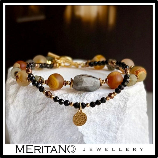 bransoletka z labradorytem i agatem z zawieszką oraz cienka bransoletka z turmalinu leżąca na białym kamieniu bransoletka z labradorytem i agatem z zawieszką oraz cienka bransoletka z turmalinu leżąca na białym kamieniu