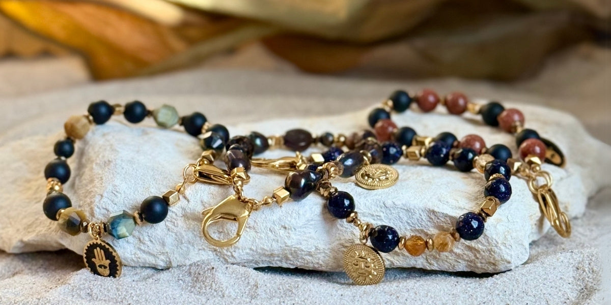 Breloczki do kluczy z kamieni i pereł leżące na kamieniu i piasku. Meritano Jewellery