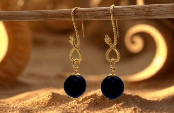 Kolczyki z czarnym onyksem i złotym wężem na tle pustynnych piasków