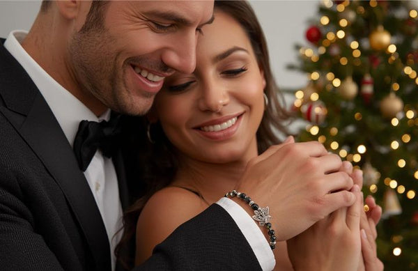 Mężczyzna w eleganckim garniturze z bransoletką z czarnych kamieni naturalnych obejmuje kobietę przy świątecznej choince.