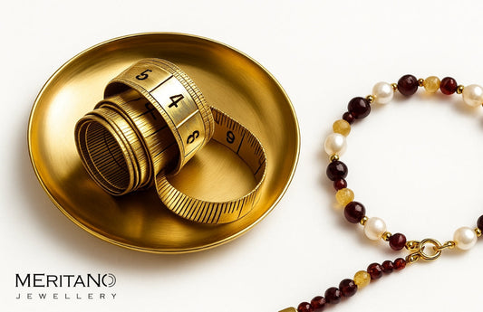 miarka krawiecka leżąca na złotym talerzu a obok bransoletka z kamieni naturalnych i pereł.