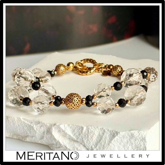 Bransoletka z kryształem górskim i turmalinem, ze złotymi elementami, leżąca na białym kamieniu