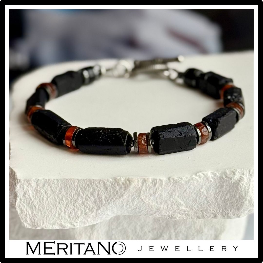 Męska bransoletka z czarnym turmalinem i granatem hessonit, leżąca na białym gipsie.