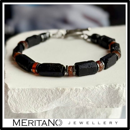 Męska bransoletka z czarnym turmalinem i granatem hessonit, leżąca na białym gipsie.