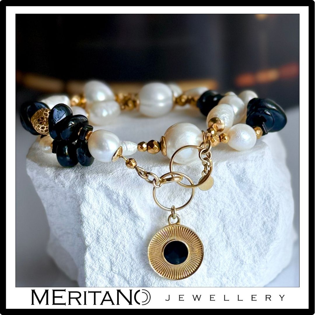 Bransoletka z pereł naturalnych z czarnym turmalinem i złotą zawieszką, leżąca na białym gipsie. Biżuteria Meritano Jewellery