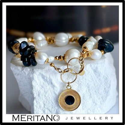 Bransoletka z pereł naturalnych z czarnym turmalinem i złotą zawieszką, leżąca na białym gipsie. Biżuteria Meritano Jewellery