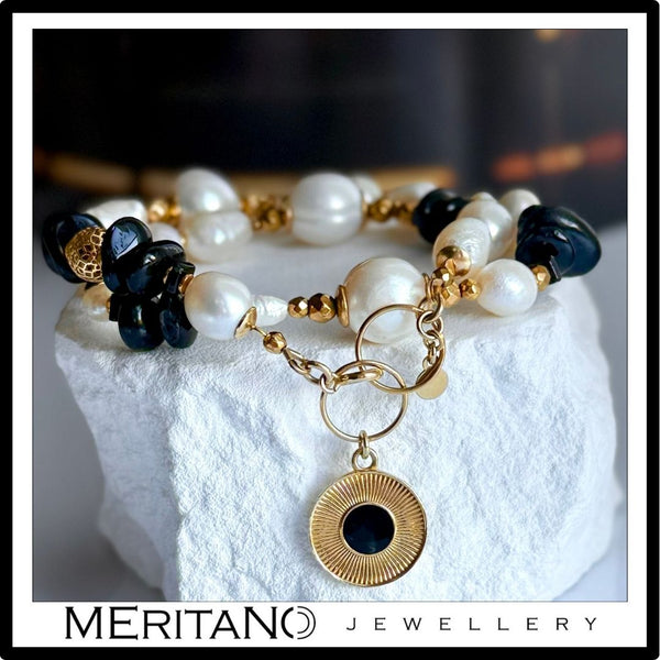 Bransoletka z pereł naturalnych z czarnym turmalinem i złotą zawieszką, leżąca na białym gipsie. Biżuteria Meritano Jewellery