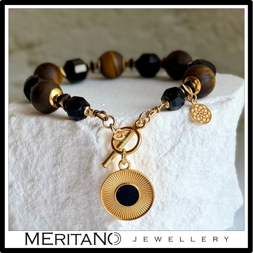 Bransoletka z czarnym turmalinem i tygrysim okiem z zawieszką, leżąca na białym kamieniu