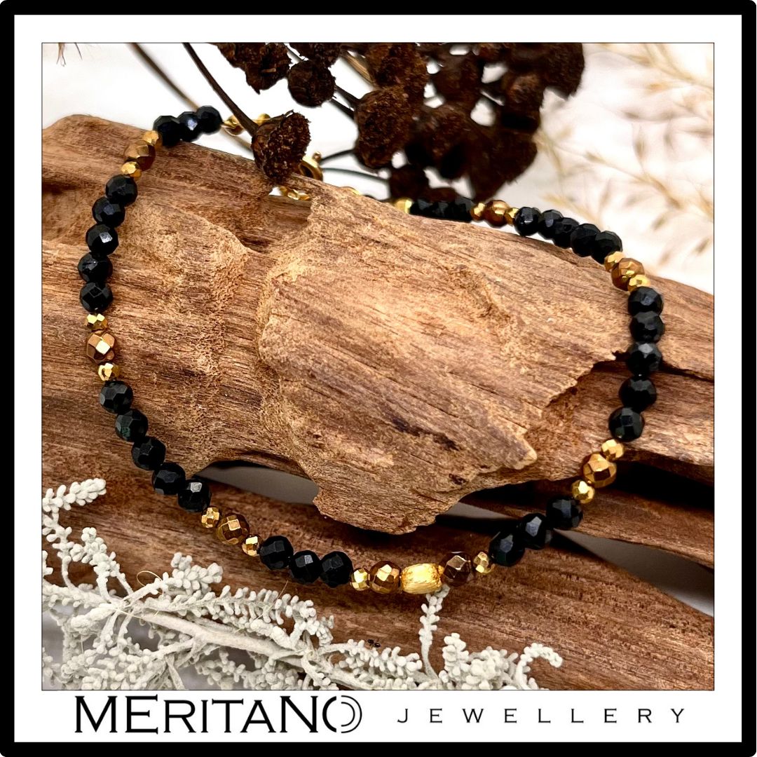 cienka czarna bransoletka z kamieni naturalnych z turmalinem, leżąca na drewnie