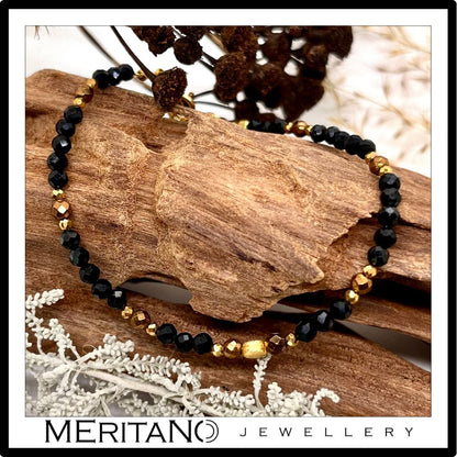 cienka czarna bransoletka z kamieni naturalnych z turmalinem, leżąca na drewnie