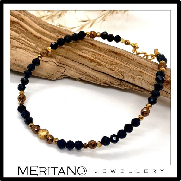 cienka czarna bransoletka z kamieni naturalnych z turmalinem, leżąca obok drewna