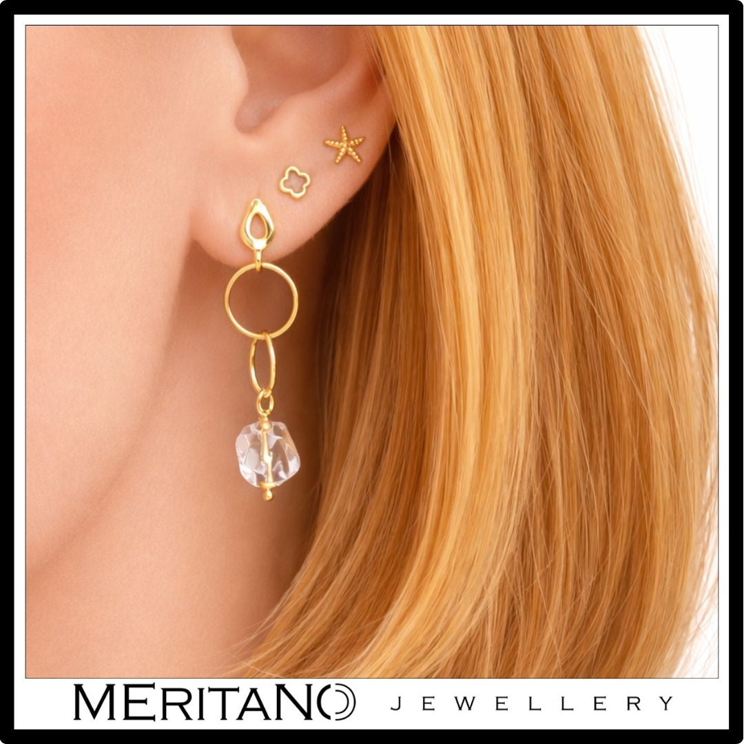 złote wiszące kolczyki z kryształem górskim na uchu