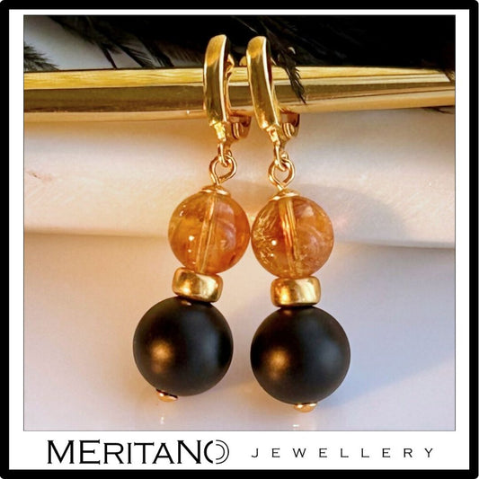 Wiszące kolczyki z onyksem i cytrynem obok czarnych piór Wiszące kolczyki z onyksem i cytrynem obok czarnych piór