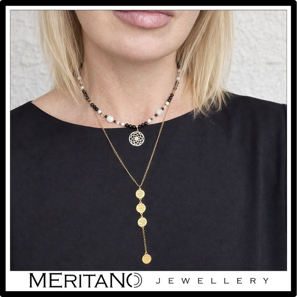 Naszyjnik z turmalinem i kamienie księżycowym w towarzystwie łańcuszka krawatki na szyi modelki w czarnej bluzce