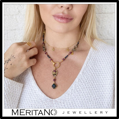 Naszyjnik krawatka z rubinem i szafirem oraz koniczyną z labradorytu na szyi modelki w białym swetrze