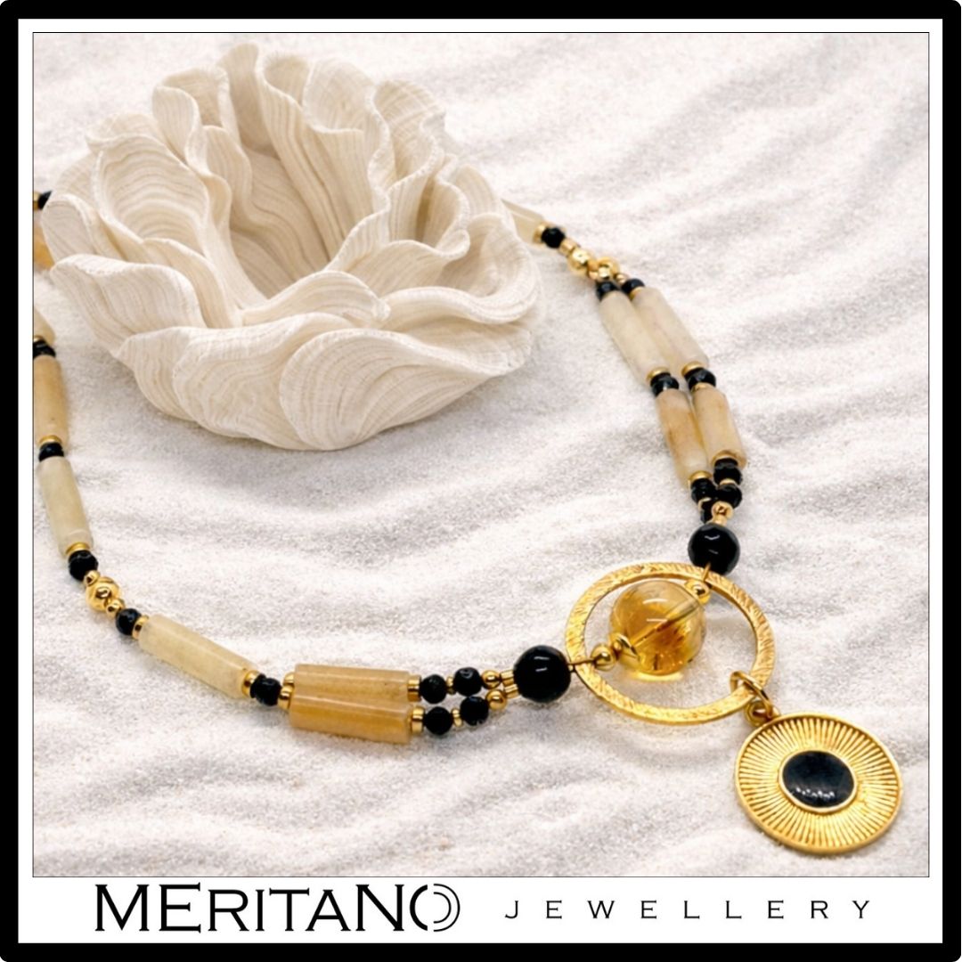 Naszyjnik z kwarcem, turmalinem i cytrynem z czarną złotą zawieszką leżący na białym piasku