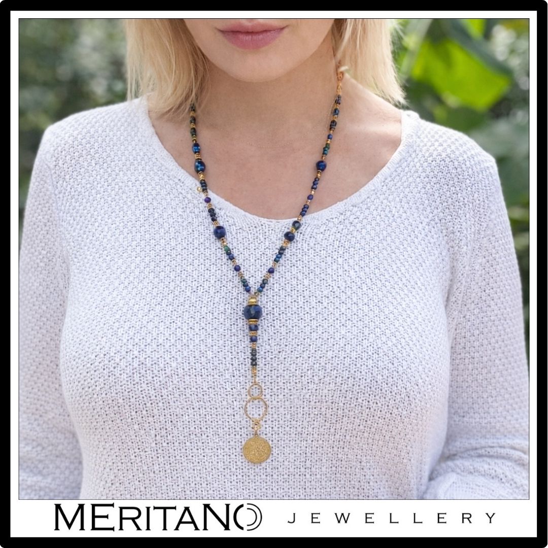 Długi, niebieski naszyjnik lapis lazuli, azuryt i moneta na szyi modelki w białym swetrze