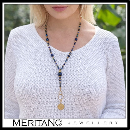 Długi, niebieski naszyjnik lapis lazuli, azuryt i moneta na szyi modelki w białym swetrze