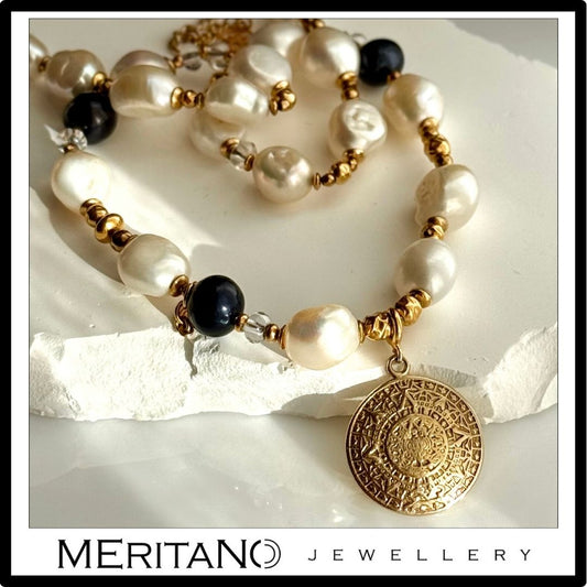 Naszyjnik perły barokowe ze złotą zawieszką - monetą Azteków, leżący na białym kamieniu Naszyjnik perły barokowe ze złotą zawieszką - monetą Azteków, leżący na białym kamieniu