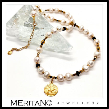 Naszyjnik z drobnych pereł naturalnych ze złotą zawieszką obok szkła