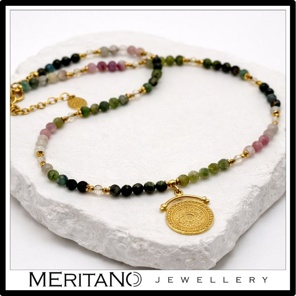 Naszyjnik z kolorowym turmalinem i złotą zawieszką boho leżący na białej tacy