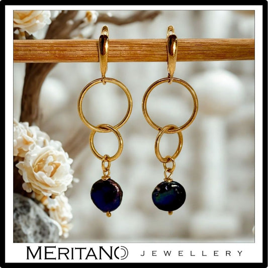 Wiszące kolczyki z czarną perłą obok kwiatów Wiszące kolczyki z czarną perłą obok kwiatów